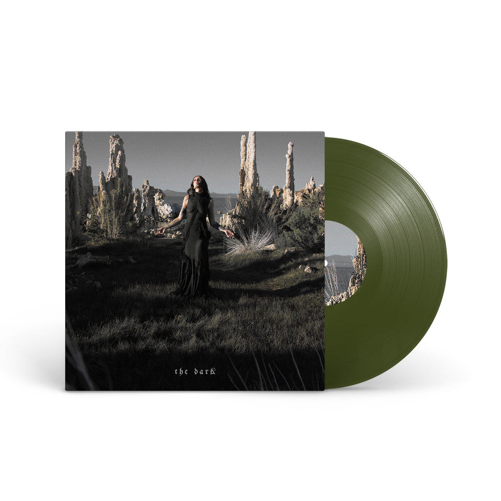 Chelsea Wolfe - The Dark (Forest Green) Vinyl A vinyl record partially pulled from its sleeve, showing an album cover with a dark landscape scene and a translucent olive green record on a white background.
