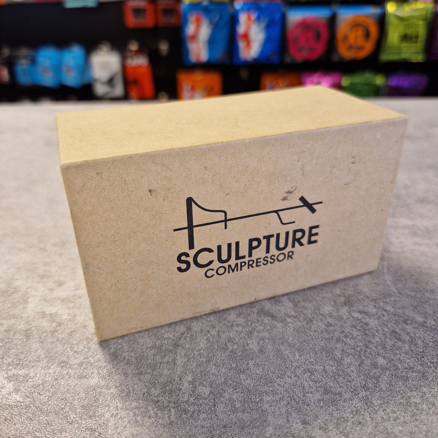 Cardboard packaging with 'Sculpture Compressor' logo on a textured surface.