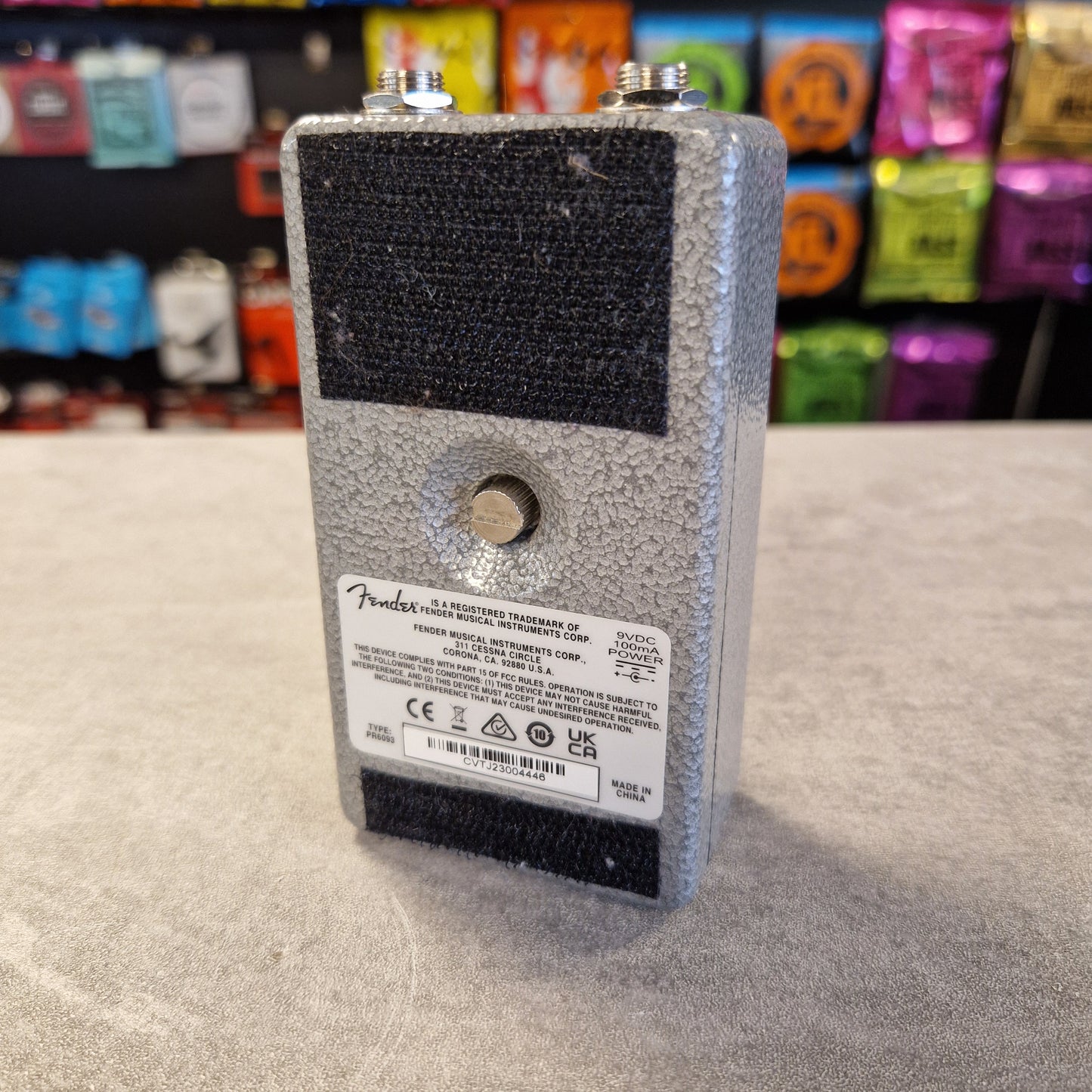 Fender Hammertone Space Delay electronic device with a label on a textured surface, colourful items in the background