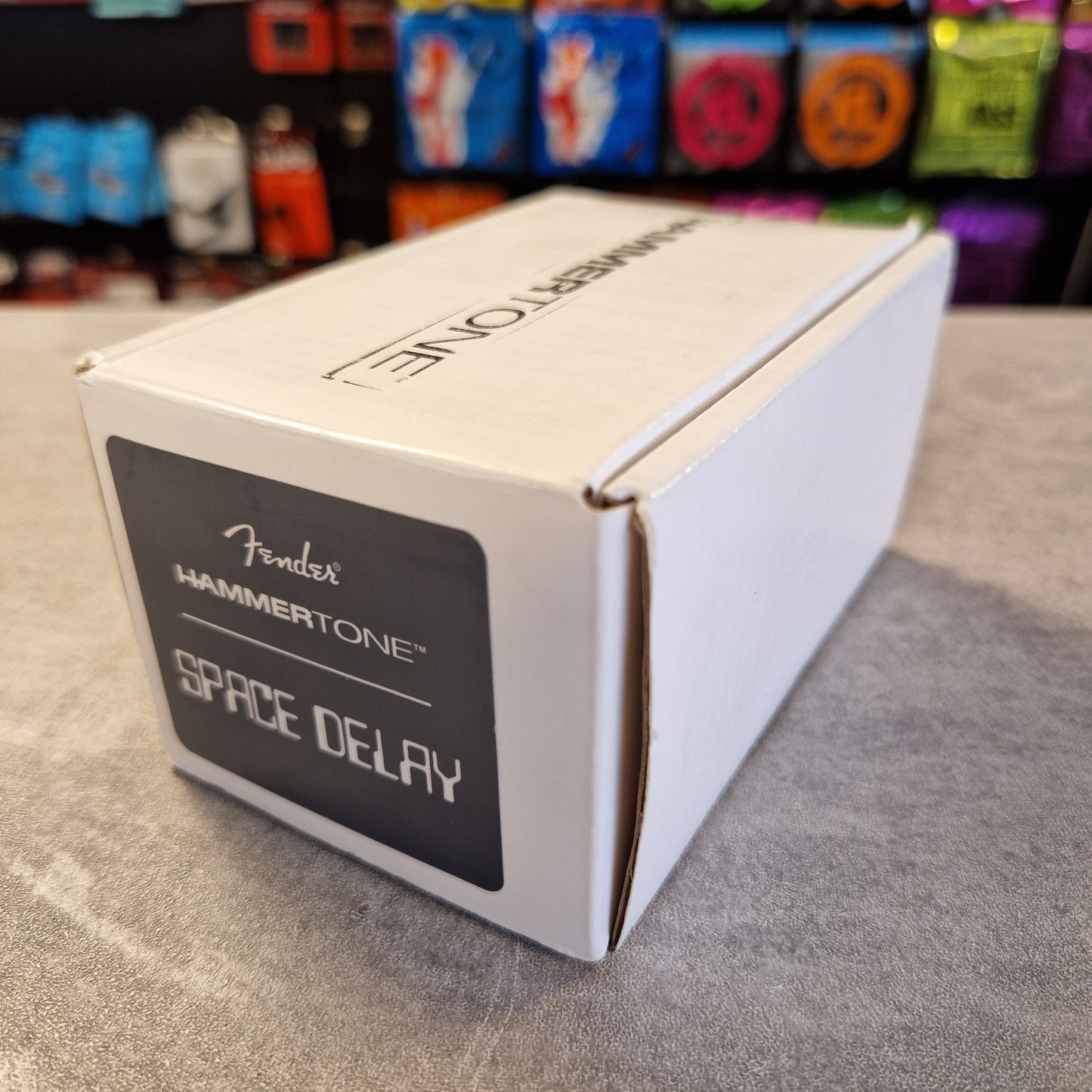 Fender Hammertone Space Delay pedal packaging on a gray surface with colorful background