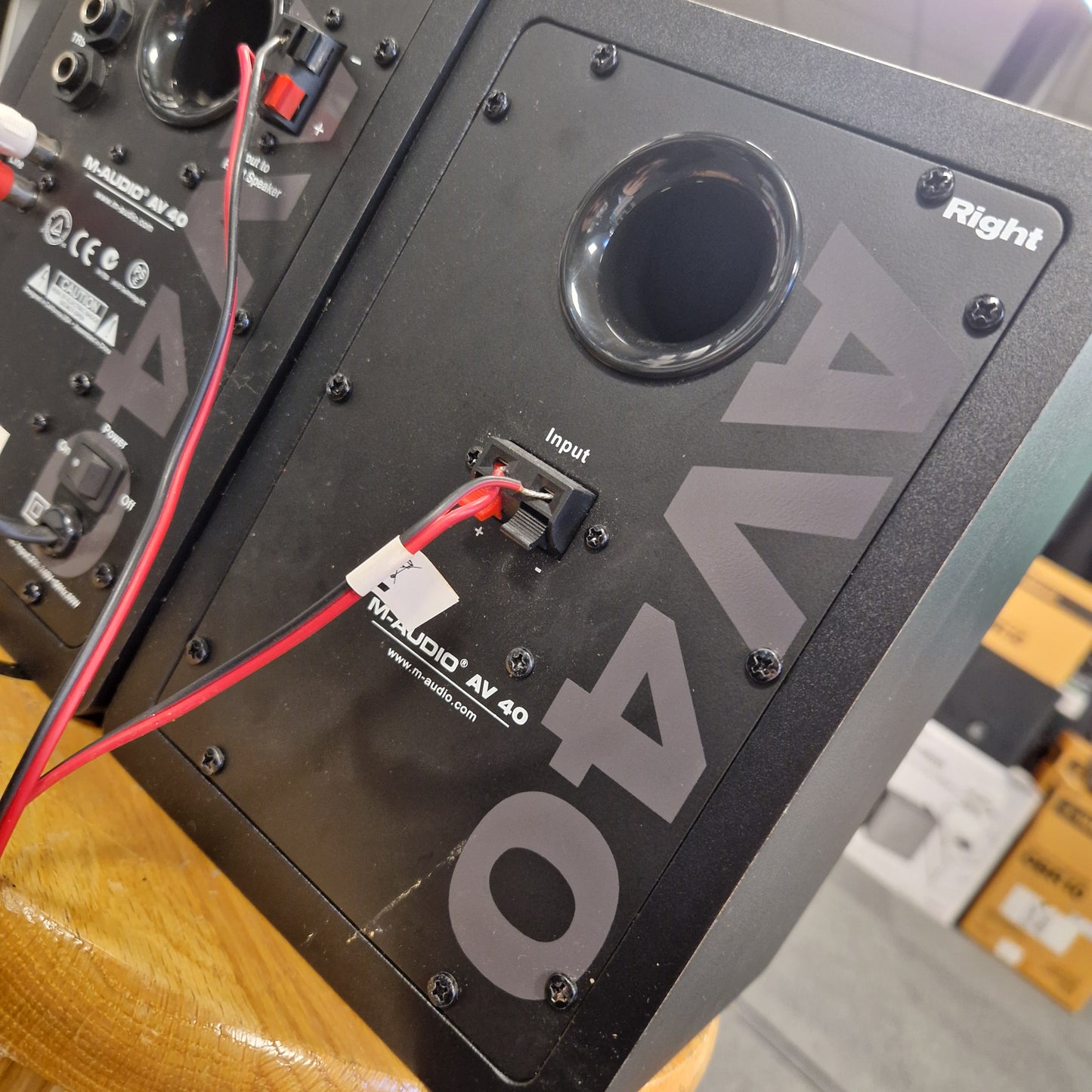 Pre-Owned M-Audio AV40 Studio Monitors Back view of an audio equipment unit with 'AV40' branding on a wooden surface.