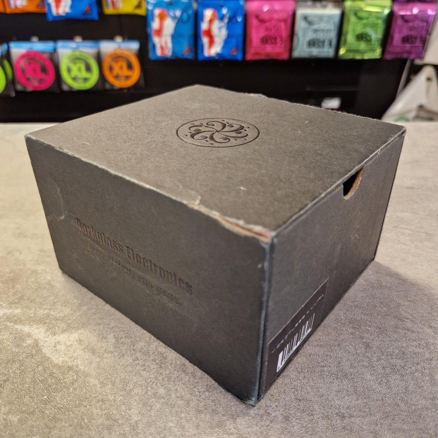 Pre-Owned Darkglass Black box with a logo on a gray surface, with colorful items in the background