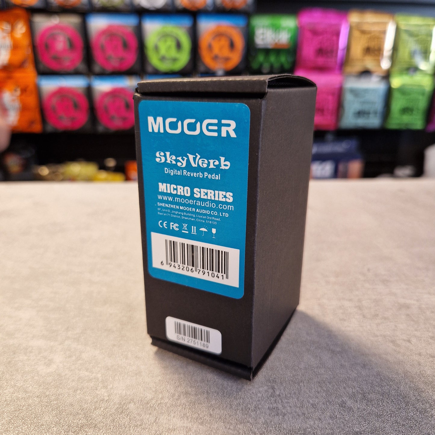 Pre-Owned Mooer MRV2 Mooer guitar effects pedal box on a gray surface with colorful boxes in the background