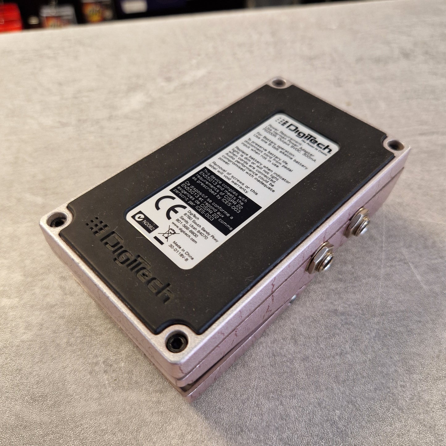 Pre-Owned Digitech Grunge Logitech electronic component with a black faceplate, silver screws, and a white product label, photographed on a gray textured surface.