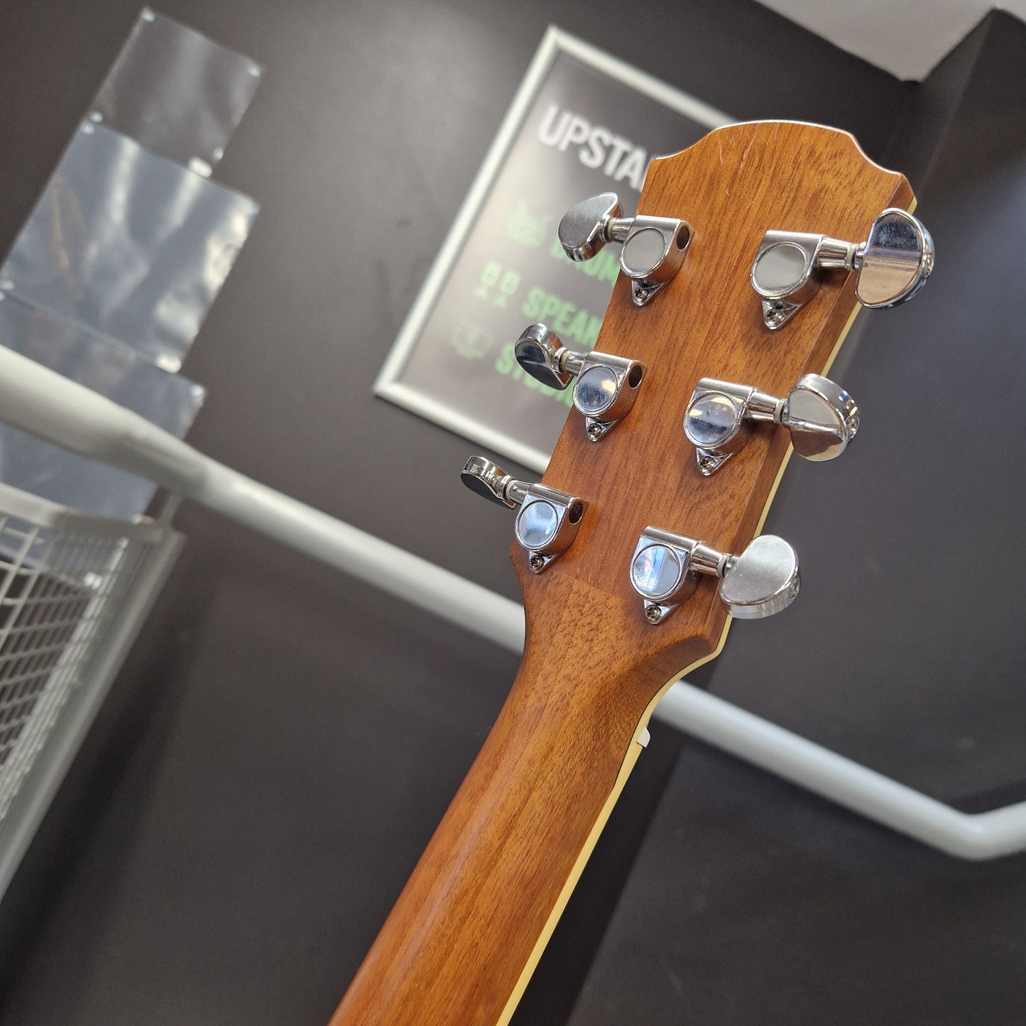 Pre-Owned Yamaha CPX700 Close-up of the headstock of a wooden stringed instrument, showing six silver tuning pegs on a warm brown wood neck, photographed indoors against a dark gray background.