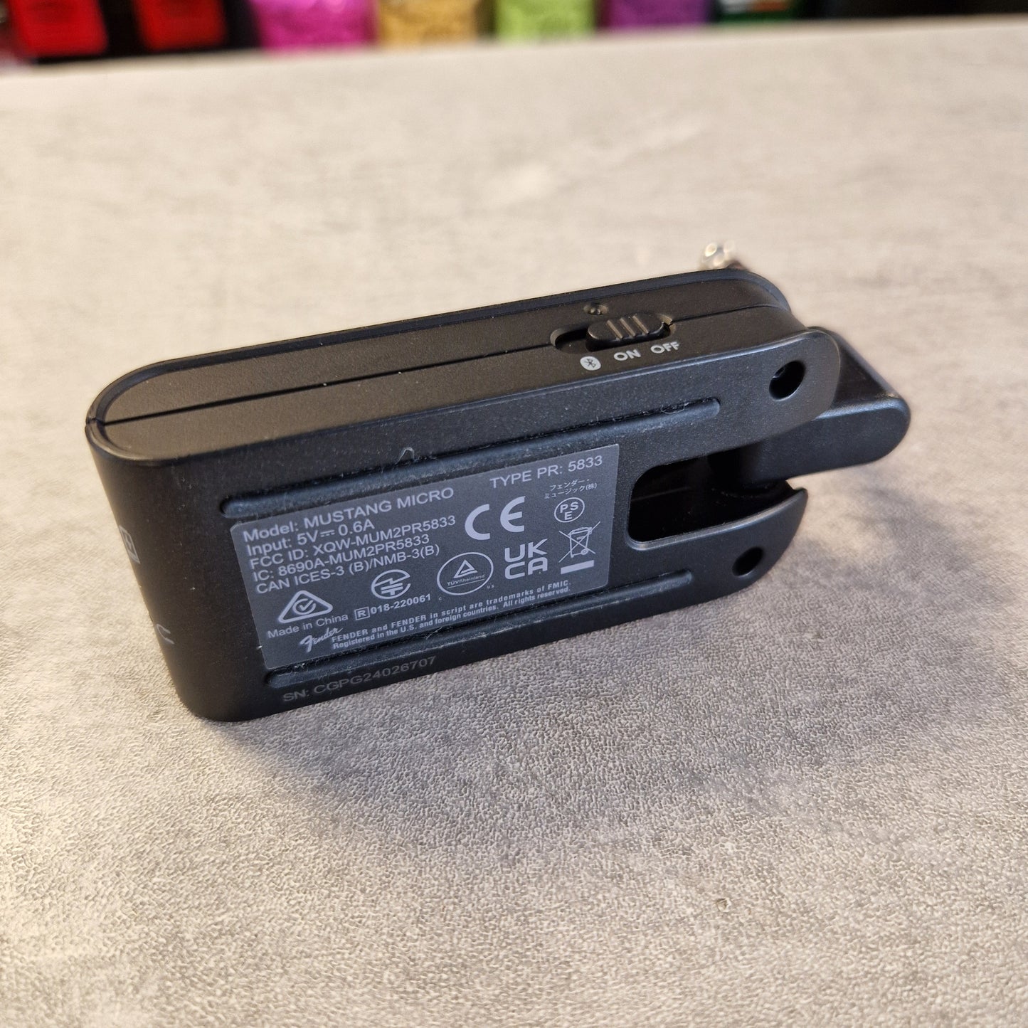 Pre-Owned Fender Mustang Micro Headphone Guitar Amplifier A black handheld electric nail gun shown from the back, displaying the model 'MUSTANG MICRO' and various regulatory stickers on its side, resting on a gray textured surface.