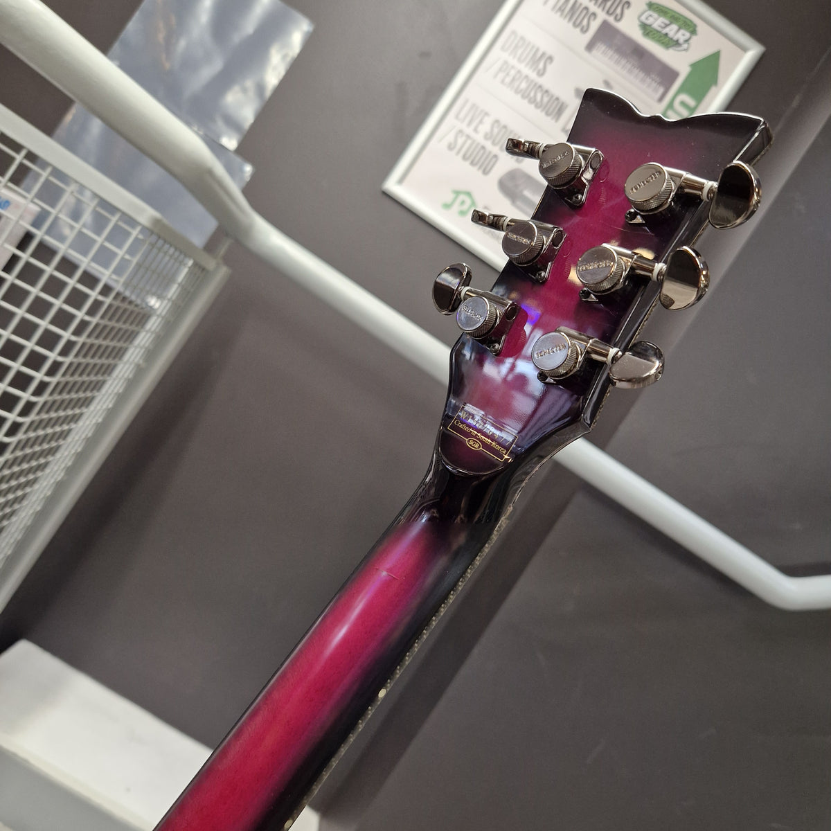 Pre-Owned Schecter Hellraiser Hybrid Solo-II Electric - Transparent Purple Burst Close-up back view of a guitar headstock and neck showing a glossy dark purple to red gradient finish, with six tuning pegs on a gray wall background.