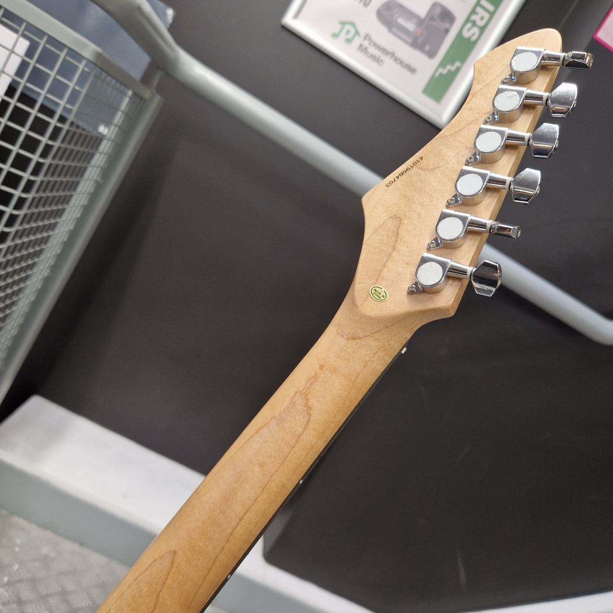 Pre-Owned Aria Pro II 714 Series Electric - Sunburst Close-up of the headstock and neck of an electric guitar, showing six silver tuning pegs, a light natural wood neck, and a small green circular logo decal on a dark display background.