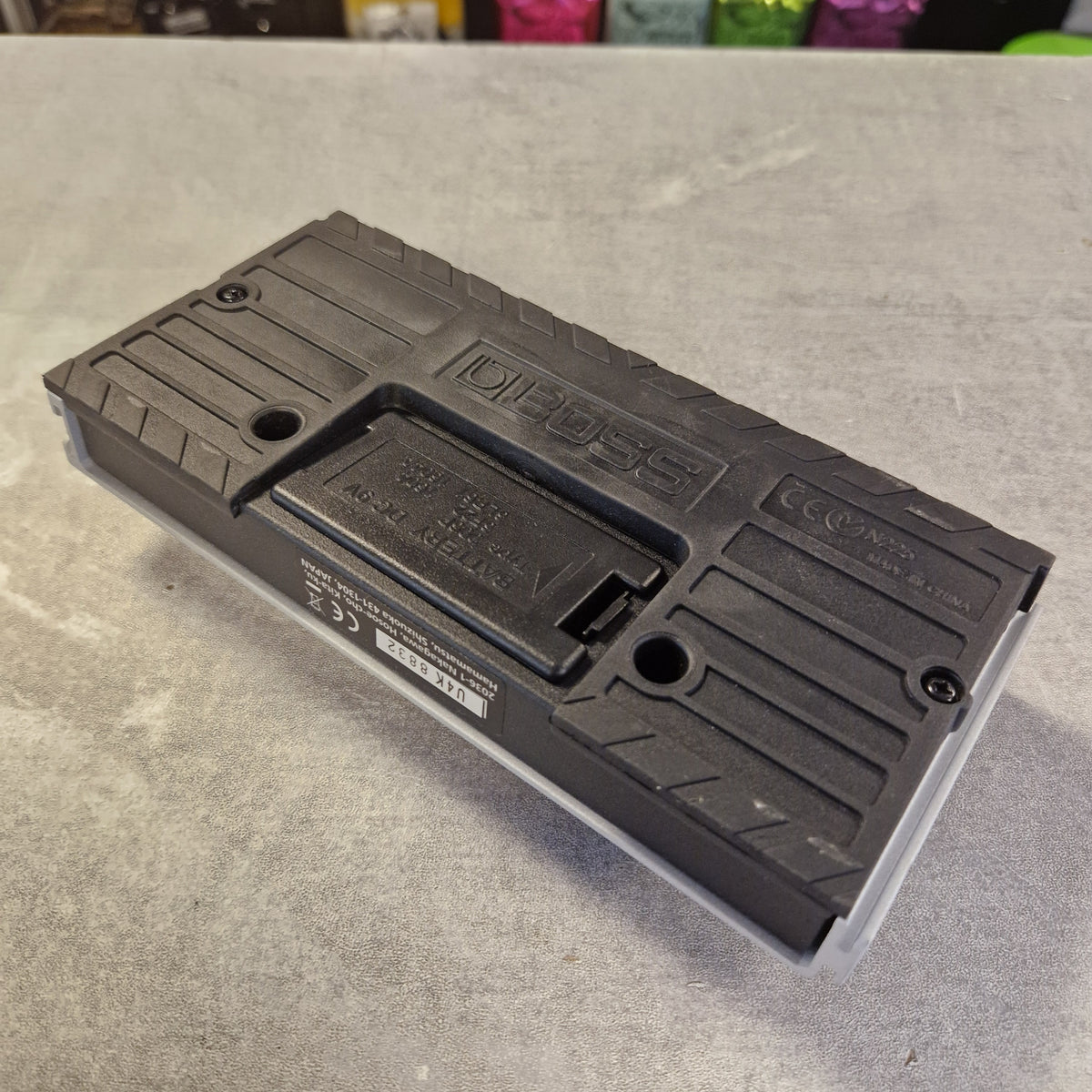 Pre-Owned Boss Dual Foot Switch FS-6 Pedal The underside of a black and gray toy battery case, showing the battery compartment, screws, and molded text, resting on a gray textured surface.