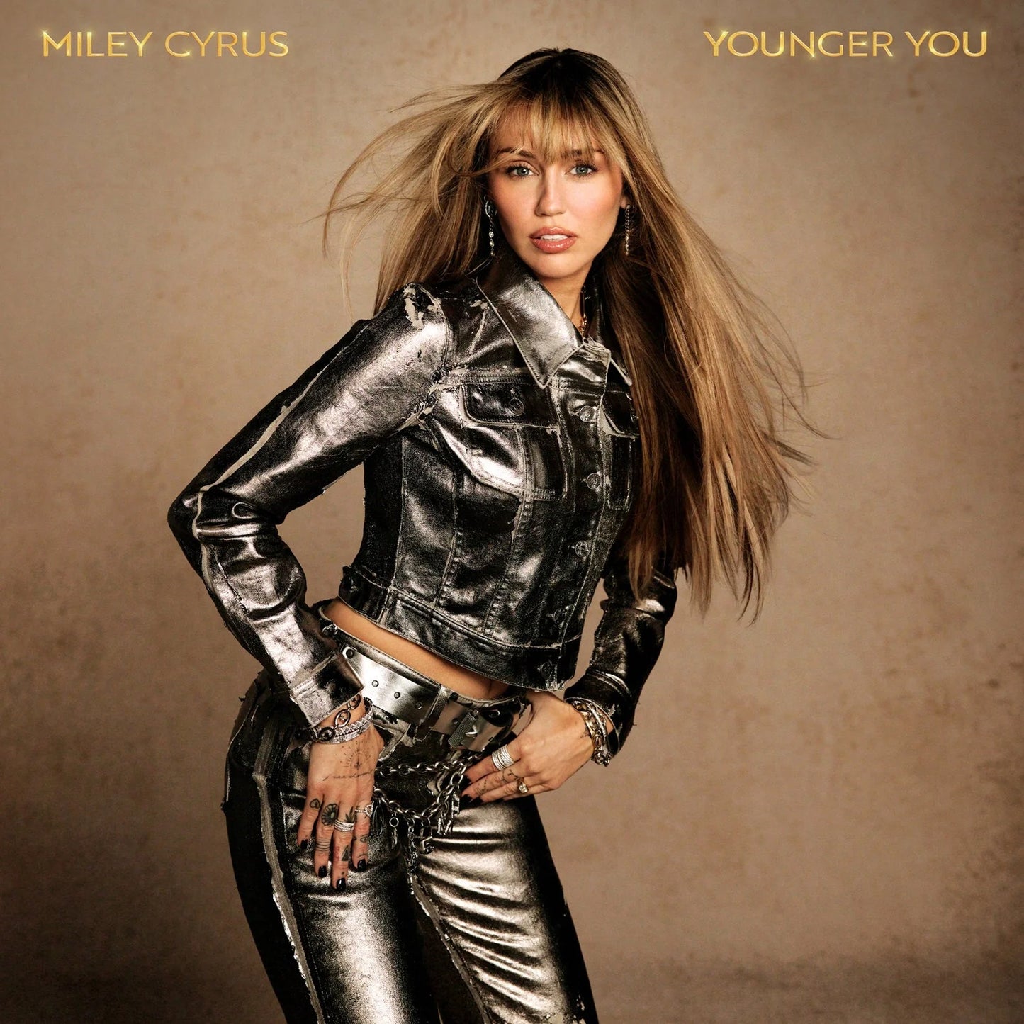 Miley Cyrus - Younger You (Limited Edition Translucent Clear) 7" Single Vinyl Miley Cyrus in a metallic silver cropped leather jacket and matching metallic pants against a warm beige studio background, with 'MILEY CYRUS' and 'YOUNGER YOU' text at the top corners.