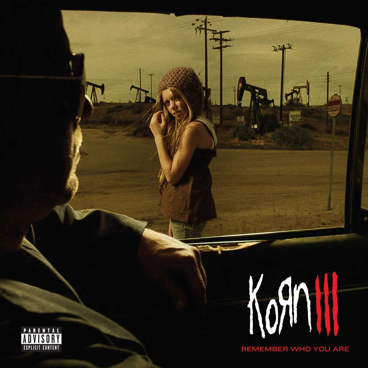 Korn - Korn III: Remember Who You Are Vinyl Album cover art for Korn III featuring a man in a car looking out at a woman standing in an open desert area with oil pumpjacks under a yellow-tinted sky. The text 'Korn III' and 'Remember Who You Are' are visible, along with a Parental Advisory label.