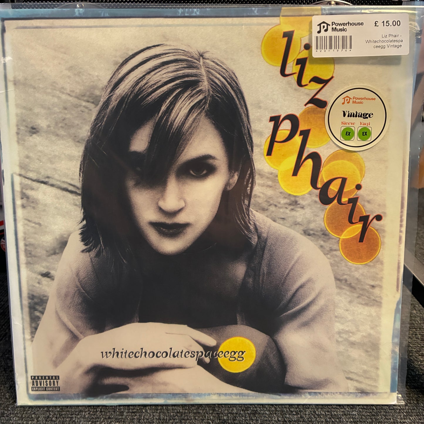Liz Phair - Whitechocolatespaceegg Vintage Vinyl LP A vinyl record sleeve for Liz Phair's album 'White Chocolatespace Egg' in a clear plastic protective case. The cover features a black and white portrait of the artist with yellow circular accents and stylized text.
