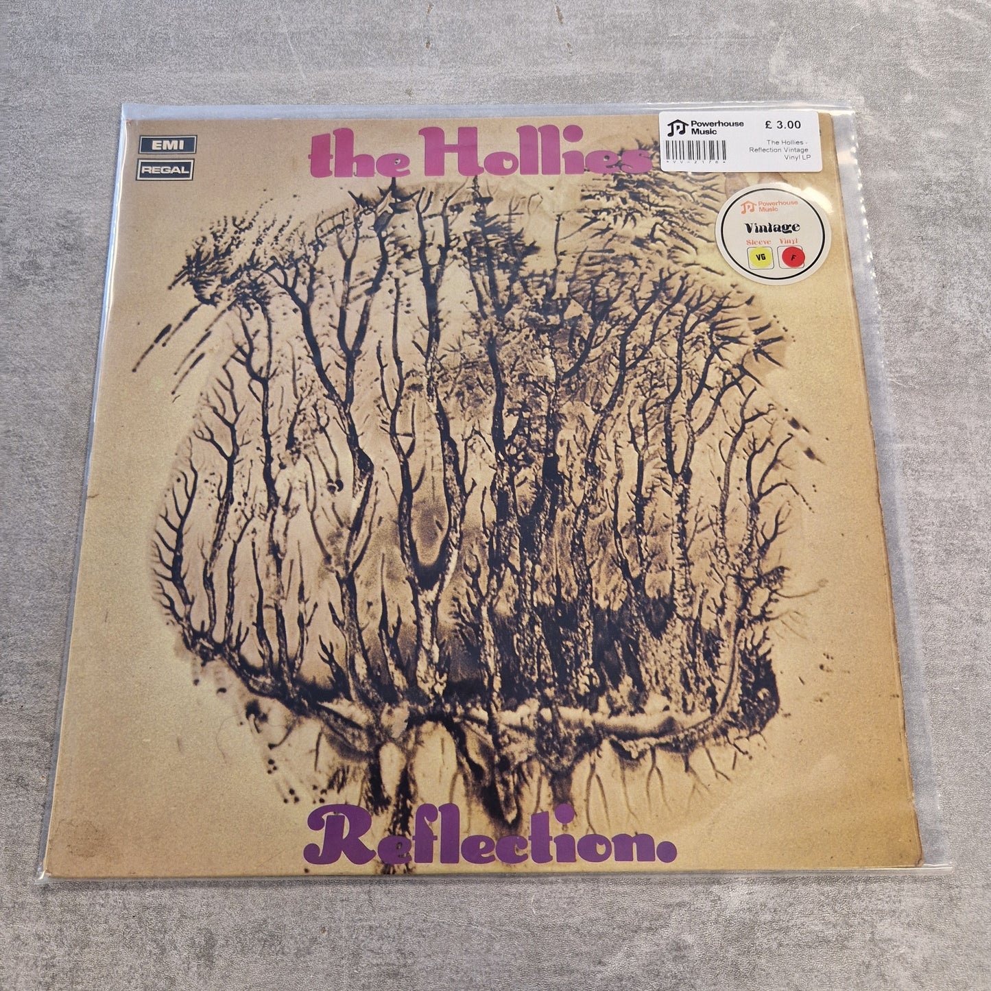 The Hollies - Reflection Vintage Vinyl LP The Holliac 'Reflection' vinyl record album cover, sealed in a clear protective plastic sleeve and photographed on a gray textured surface. The cover features a beige background with a dark brown sketch of a forest and purple text.