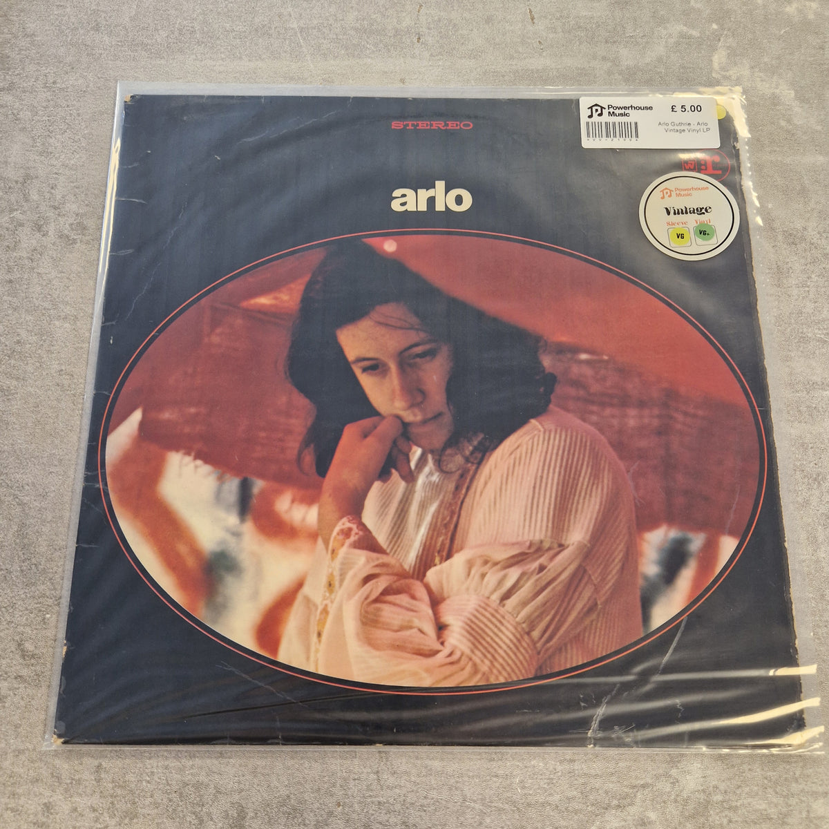 Arlo Guthrie - Arlo Vintage Vinyl LP A vinyl record sleeve for Arlo's album 'Bitter', sealed in plastic shrink wrap on a gray carpet. The cover art features a portrait of a woman under a red-orange umbrella, with the artist's name 'arlo' in white text.
