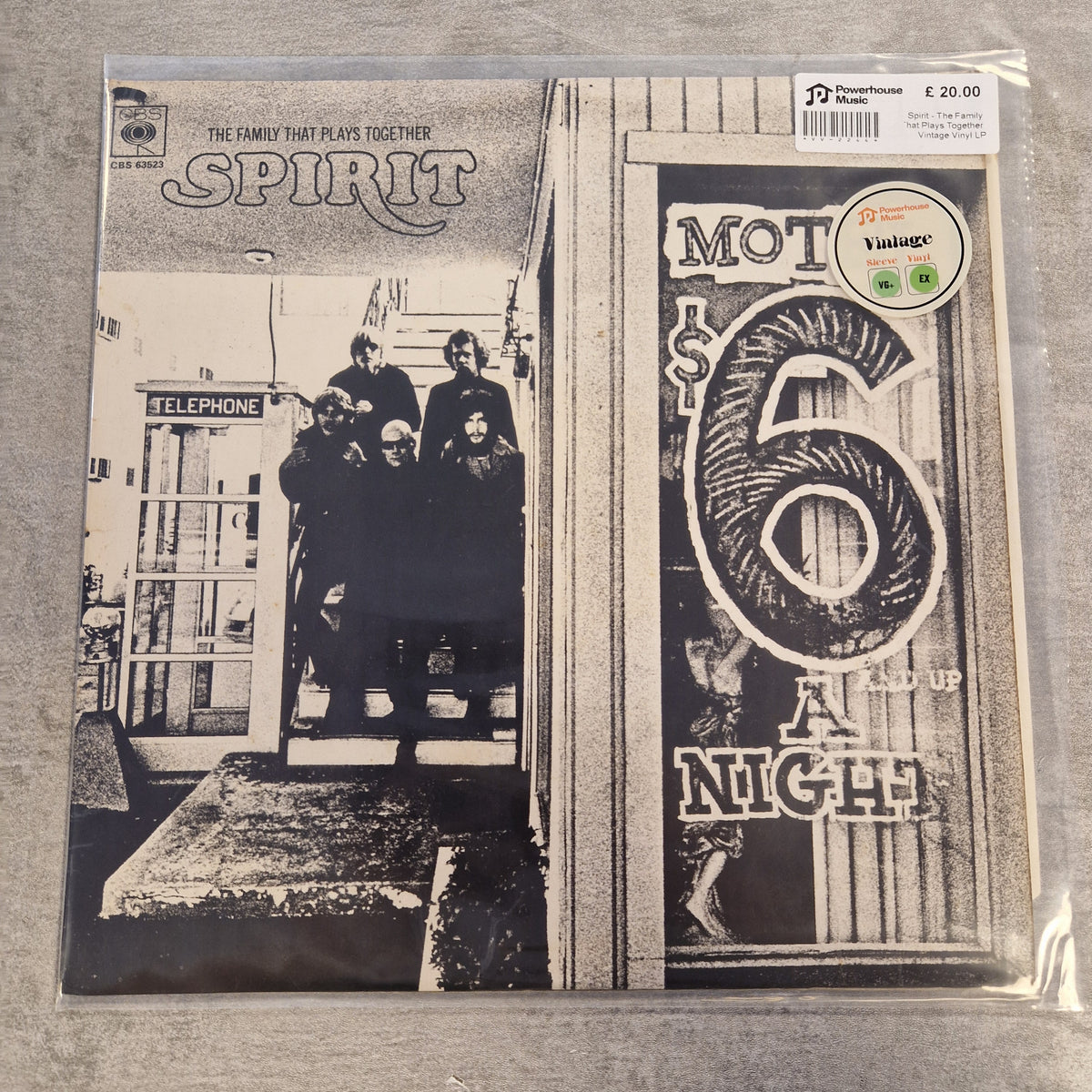 Spirit - The Family That Plays Together Vintage Vinyl LP A vinyl record sleeve for the band Spirit's 'Mot $6 A Night' is shown in its clear plastic shrink-wrap on a gray fabric surface. The cover art is black and white, featuring a group of people standing in front of a telephone booth on the left and a large stylized '6' on a storefront window on the right.
