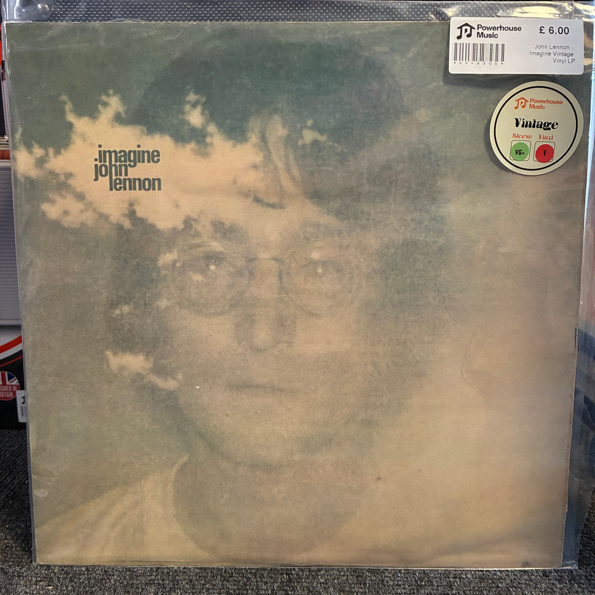 John Lennon - Imagine Vintage Vinyl LP A vinyl record sleeve for John Lennon's 'Imagine' in its clear plastic protective case. The sleeve features a faded, sepia-toned portrait of John Lennon with the album title 'imagine' and artist 'john leonard' printed on the left.