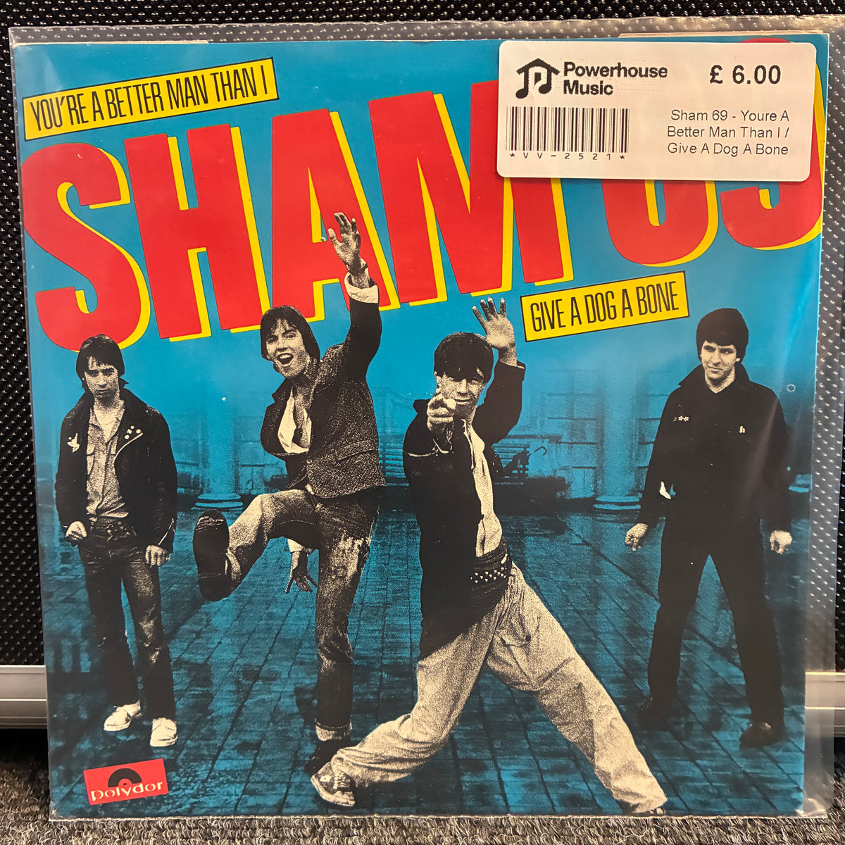 Sham 69 - You're A Better Man Than I / Give A Dog A Bone Vintage Vinyl 7" Single Shamoon's 'You're a Better Man Than I' vinyl record cover on a textured black surface, featuring a white Powerhouse Music price sticker in the top right corner.