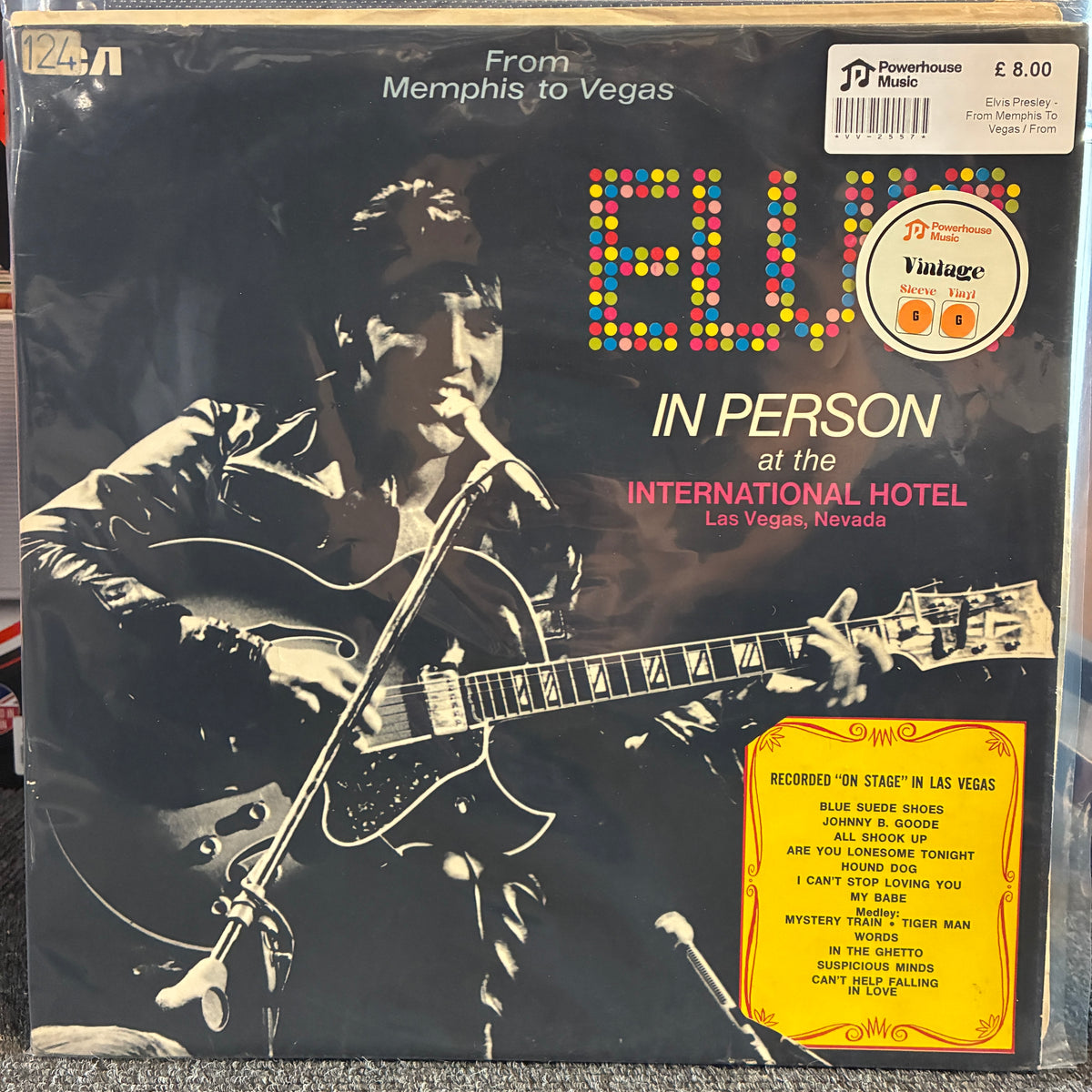 Elvis Presley - From Memphis To Vegas / From Vegas To Memphis Vintage Vinyl LP Vinyl record sleeve for Blue Eyed's 'In Person at the International Hotel' LP, featuring a black-and-white photo of a man playing an electric guitar, colorful dotted 'BLUE' lettering, and a yellow tracklist sticker on a Powerhouse label.
