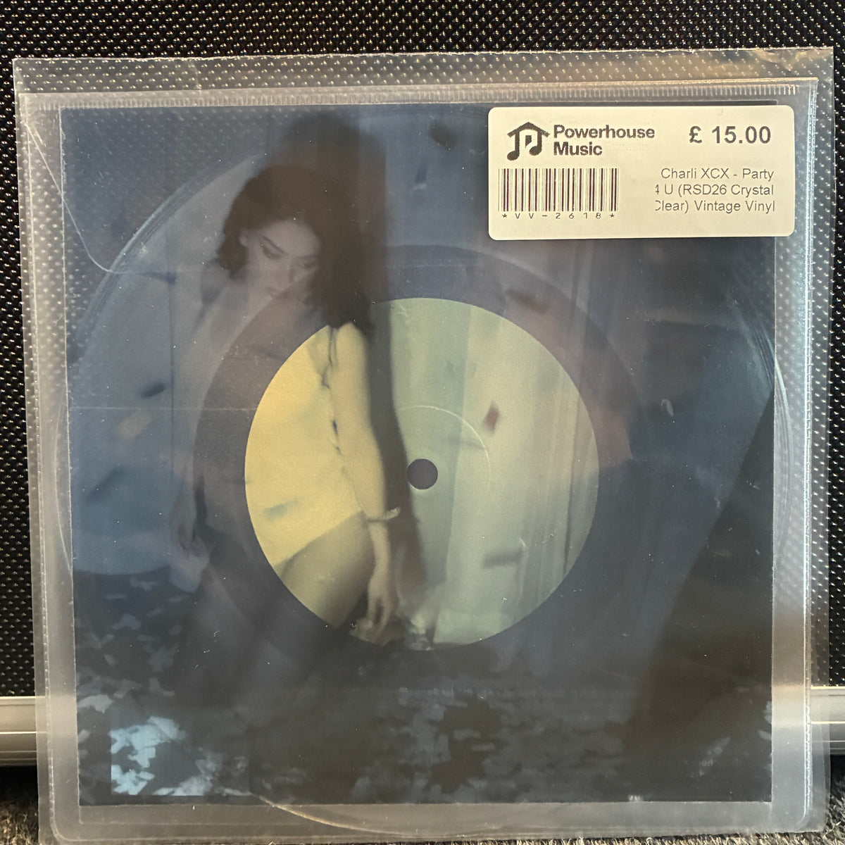 Charli XCX - Party 4 U (RSD26 Crystal Clear) Vintage Vinyl 7" Single A 12-inch vinyl record in a clear protective sleeve, featuring a dark, moody cover with a woman and a pale yellow circular center. A white sticker on the top right reads 'Powerhouse Music' and lists the track details.