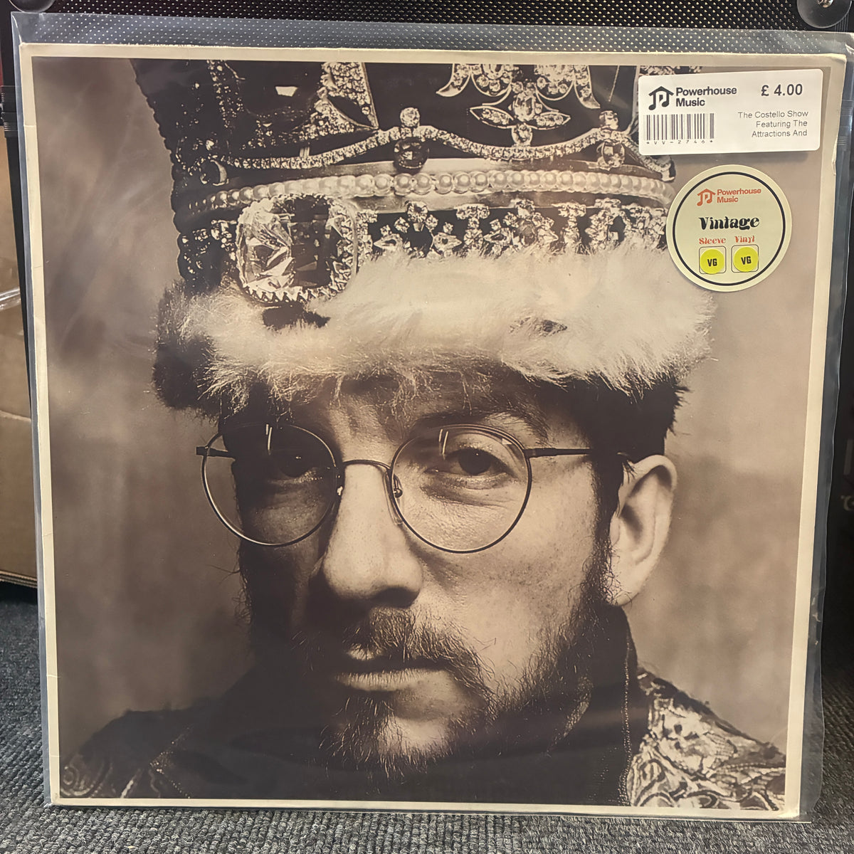 The Costello Show Featuring The Attractions And Confederates - King Of America Vintage Vinyl LP Vinyl record sleeve for The Casket Show's 'King of the Hill' album, featuring a sepia-toned portrait of a man wearing a jeweled crown and glasses. A Powerhouse logo sticker is visible in the top right corner.