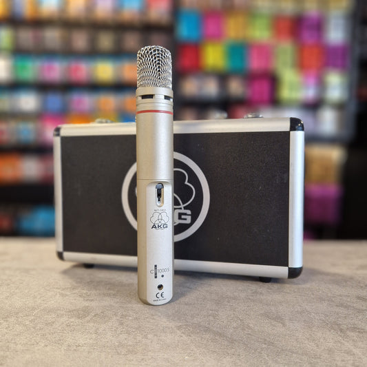 AKG C1000S Microphone with a case on a textured surface with colourful blurred background