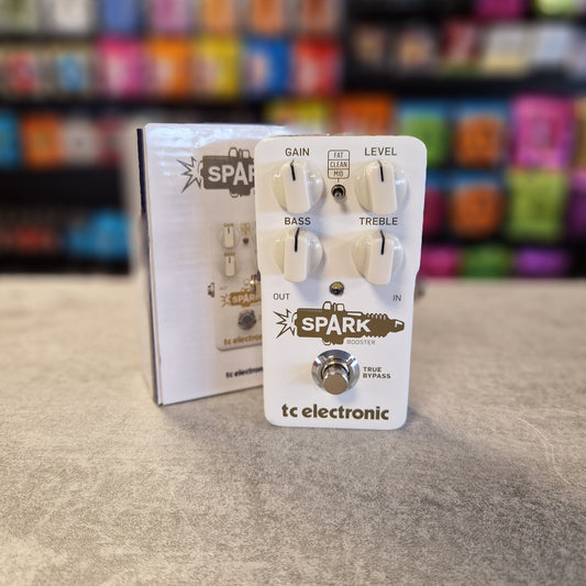 TC Electronic Spark guitar pedal on grey surface with guitar strings in background and box