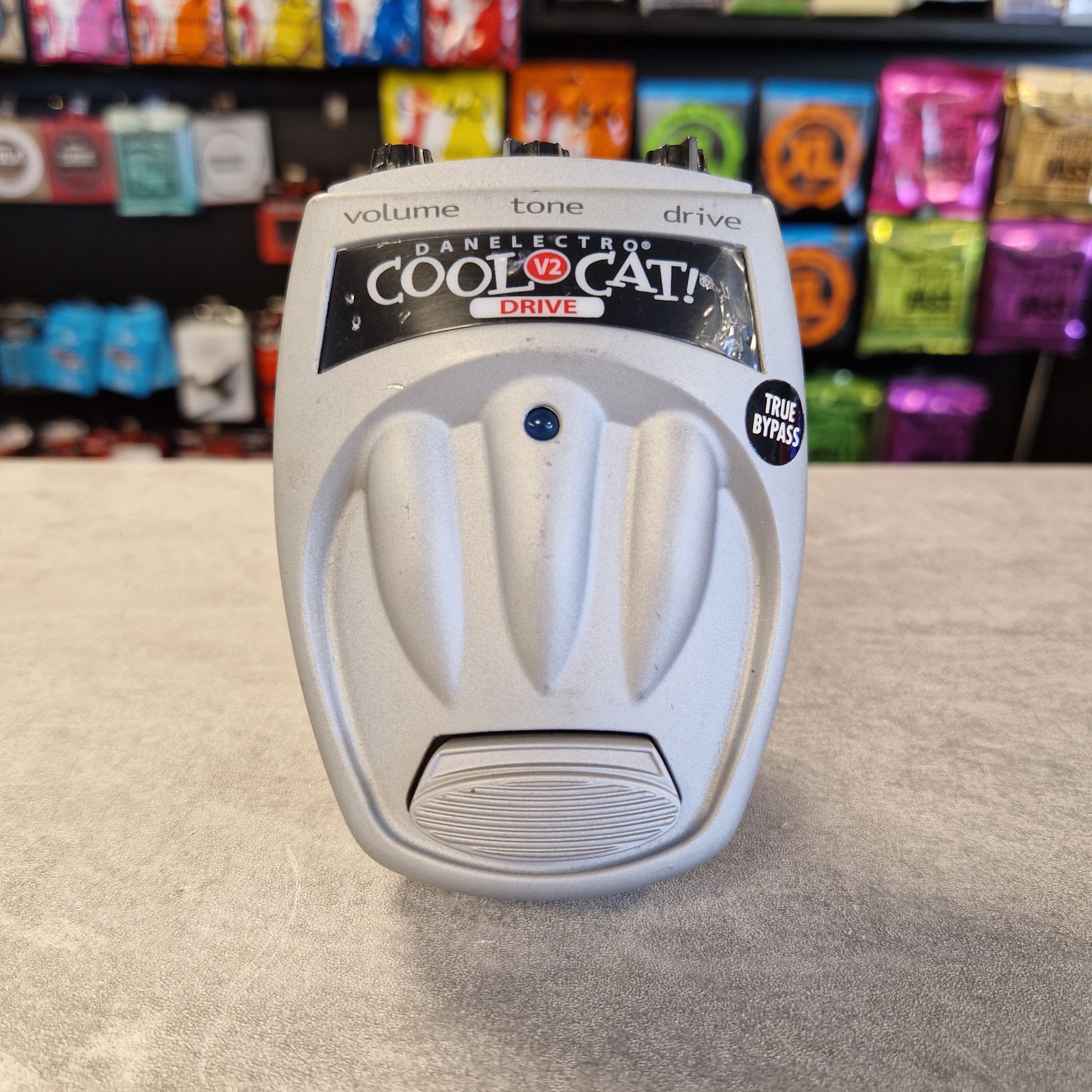 Danelectro Cool Cat V2 Drive White foot pedal switch on a gray surface with colorful packaging in the background