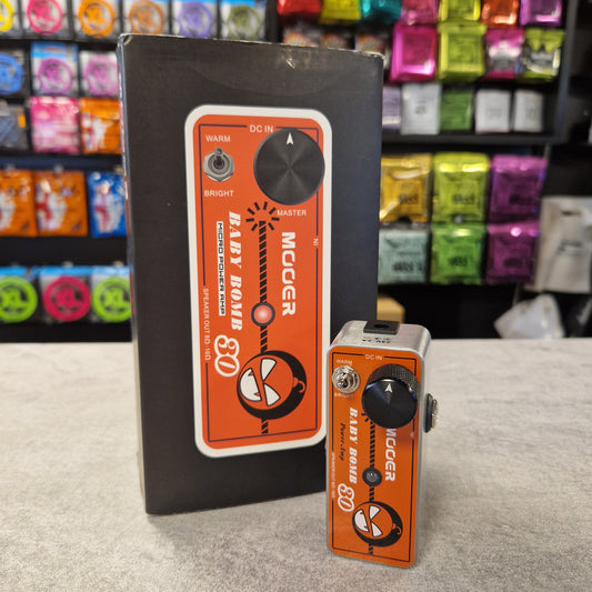 Pre-Owned Mooer Baby Bomb 30 guitar effect pedals on a grey surface with colourful boxes in the background.