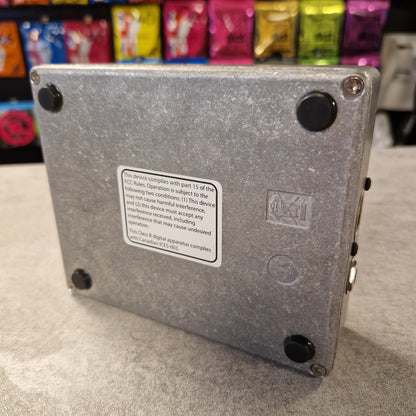 Pre-Owned Electro-Harmonix Metal box with a label on a grey surface, with colourful items in the background