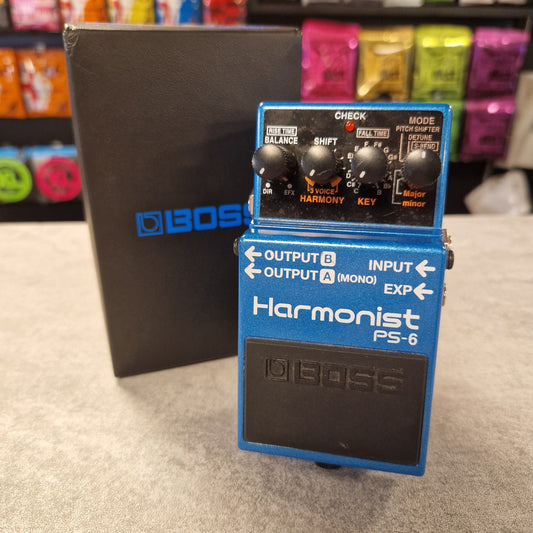 Pre-Owned Boss Harmonist PS-6 guitar effects pedal on a grey surface with colourful items in the background.
