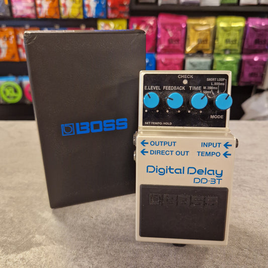 Pre-Owned Boss digital delay pedal on a grey surface with colourful boxes in the background
