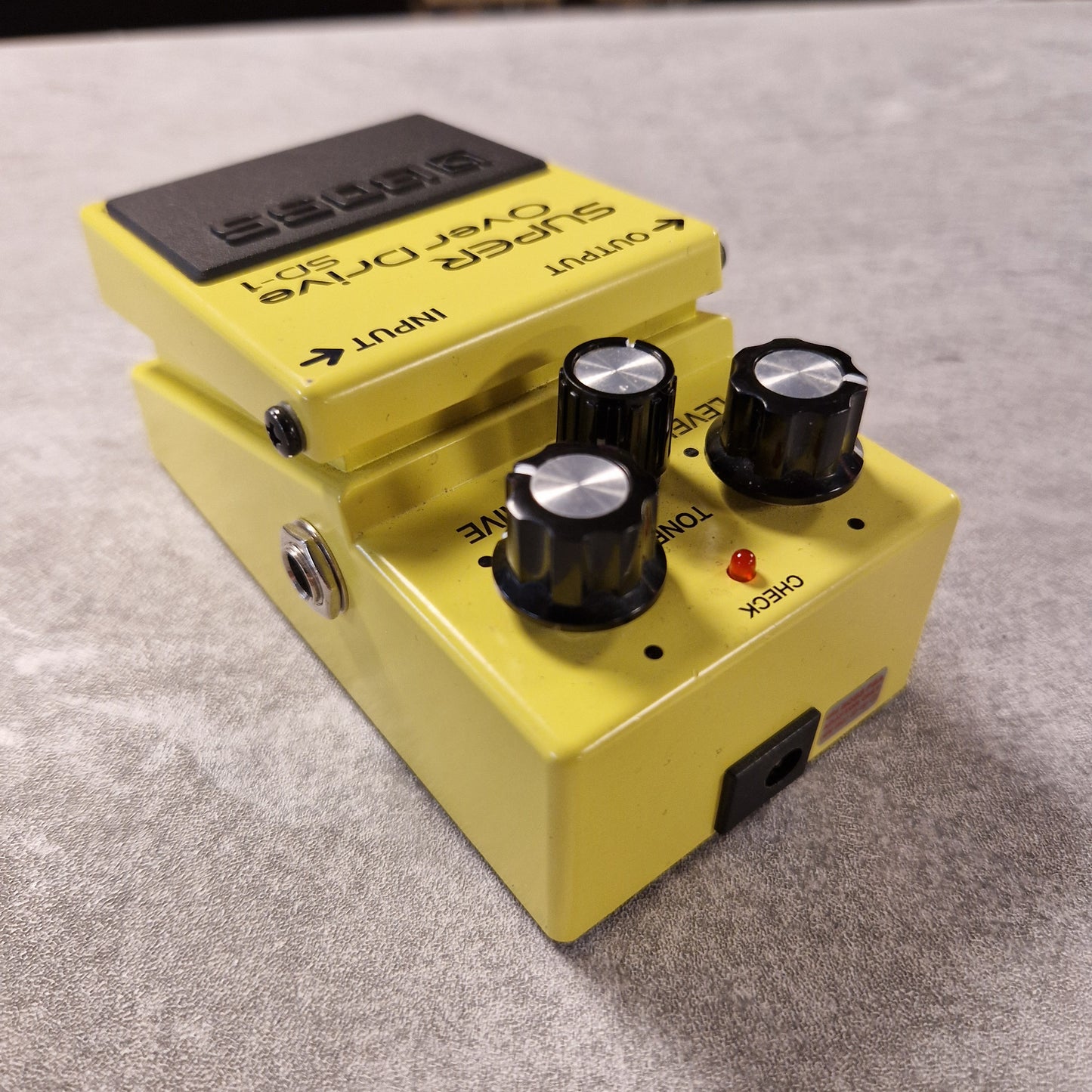 Pre-Owned Boss Yellow guitar effects pedal with knobs on a grey surface
