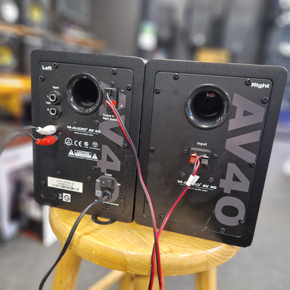 Pre-Owned M-Audio AV40 Studio Monitors Two black speakers labeled 'AV40' with visible wiring on a blurred background.