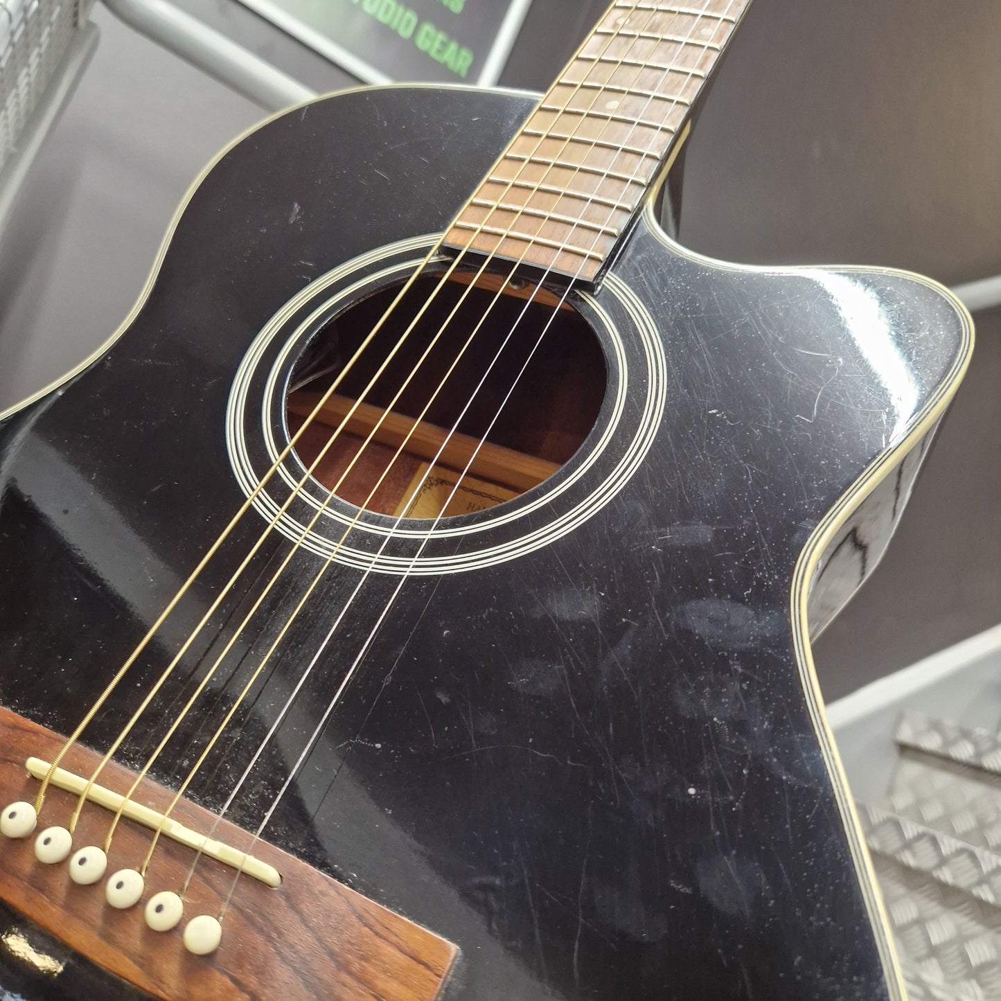 Pre-Owned Cruiser Black acoustic guitar with visible wear on the body, leaning against a metal surface.