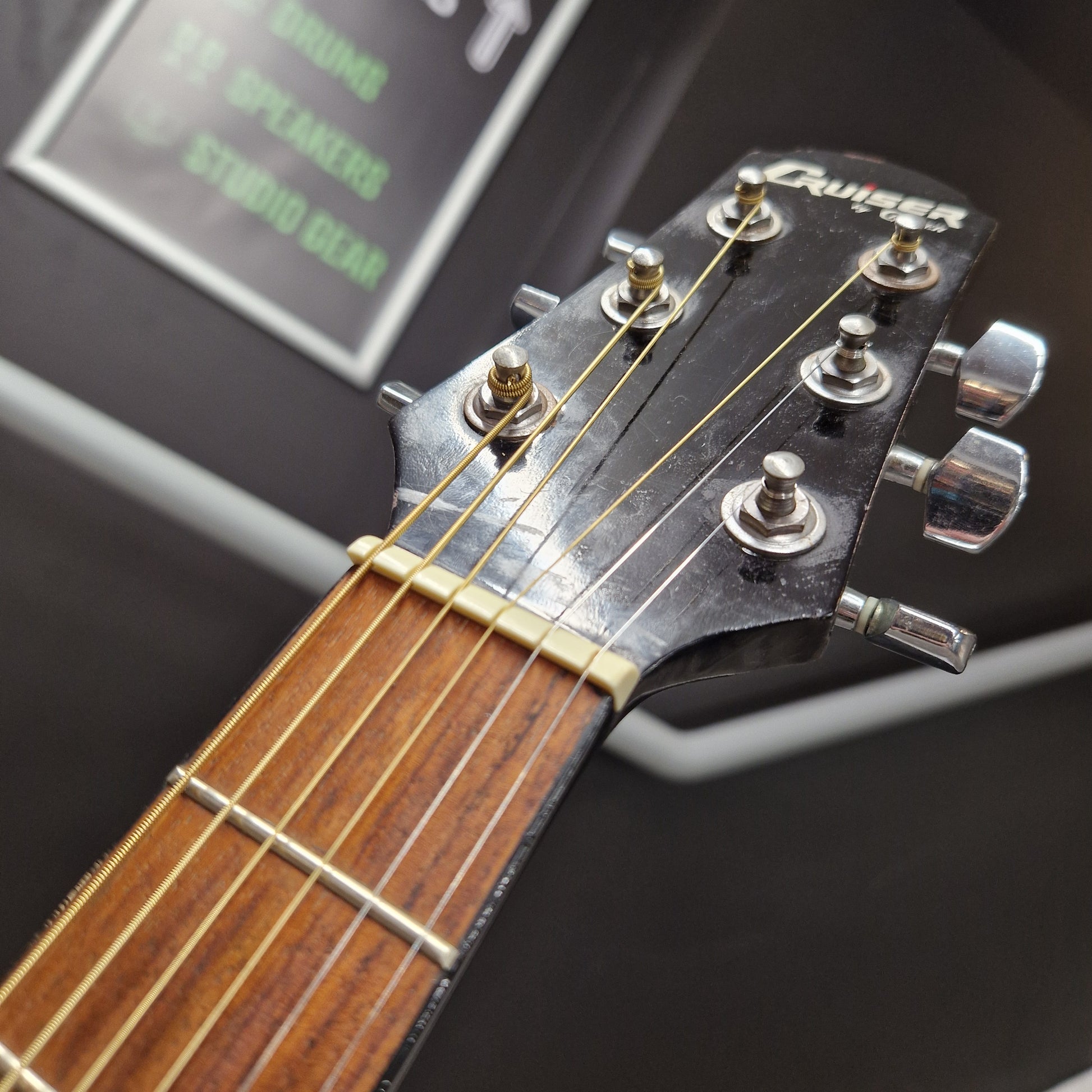 Pre-Owned Cruiser Close-up of a guitar headstock with tuning pegs and a digital tuner in the background.