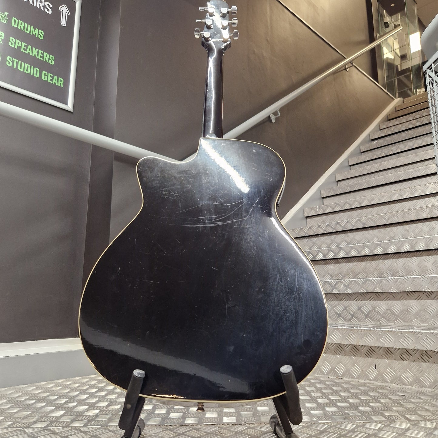 Pre-Owned Cruiser Black guitar on display in a store with a metallic surface and text in the background.