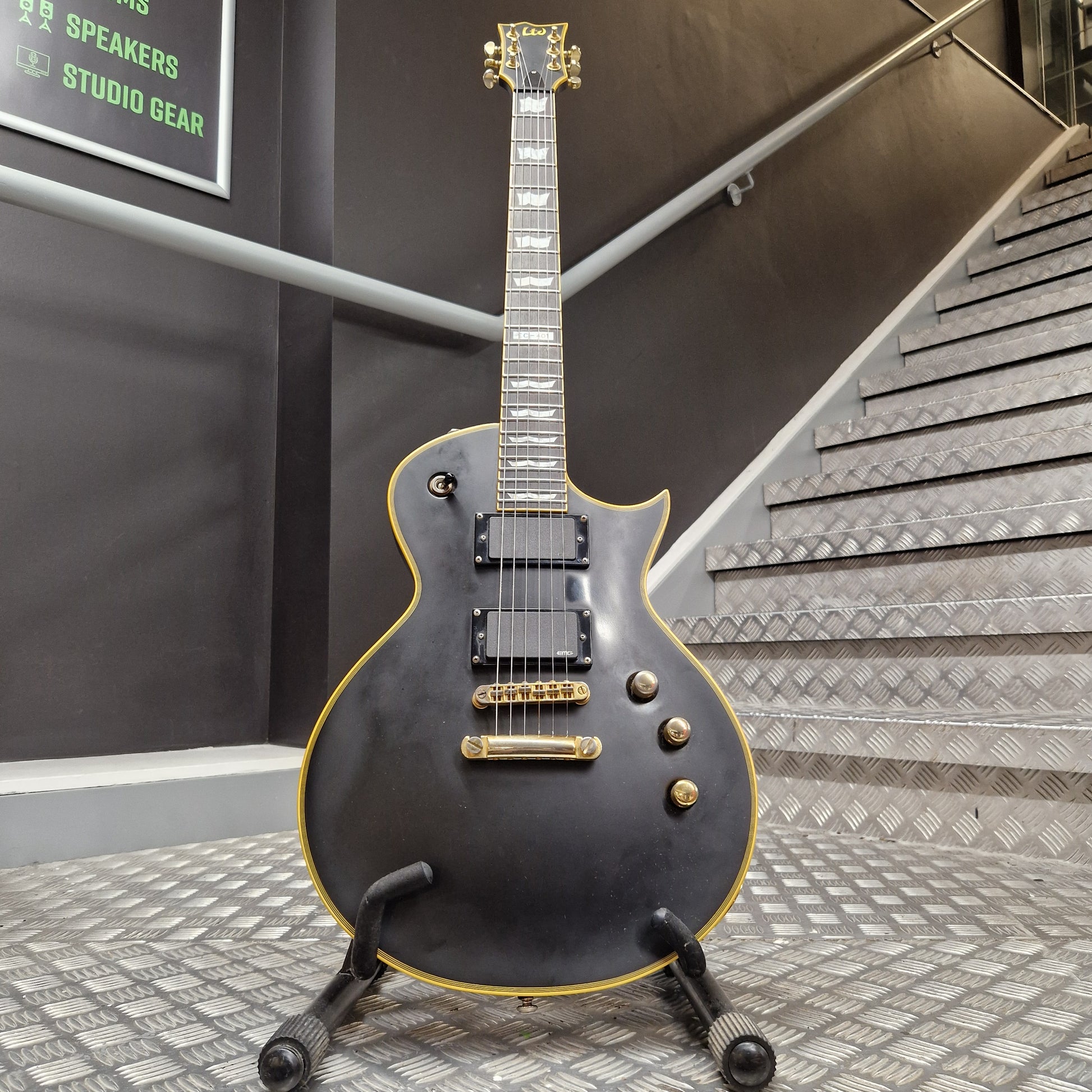 Pre-Owned ESP Black electric guitar with gold hardware on a stand in a room with acoustic panels.