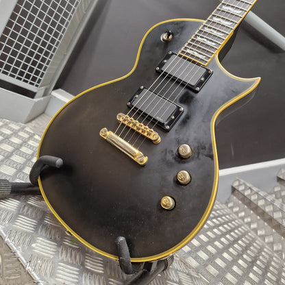 Pre-Owned ESP Black electric guitar with gold hardware on a textured surface