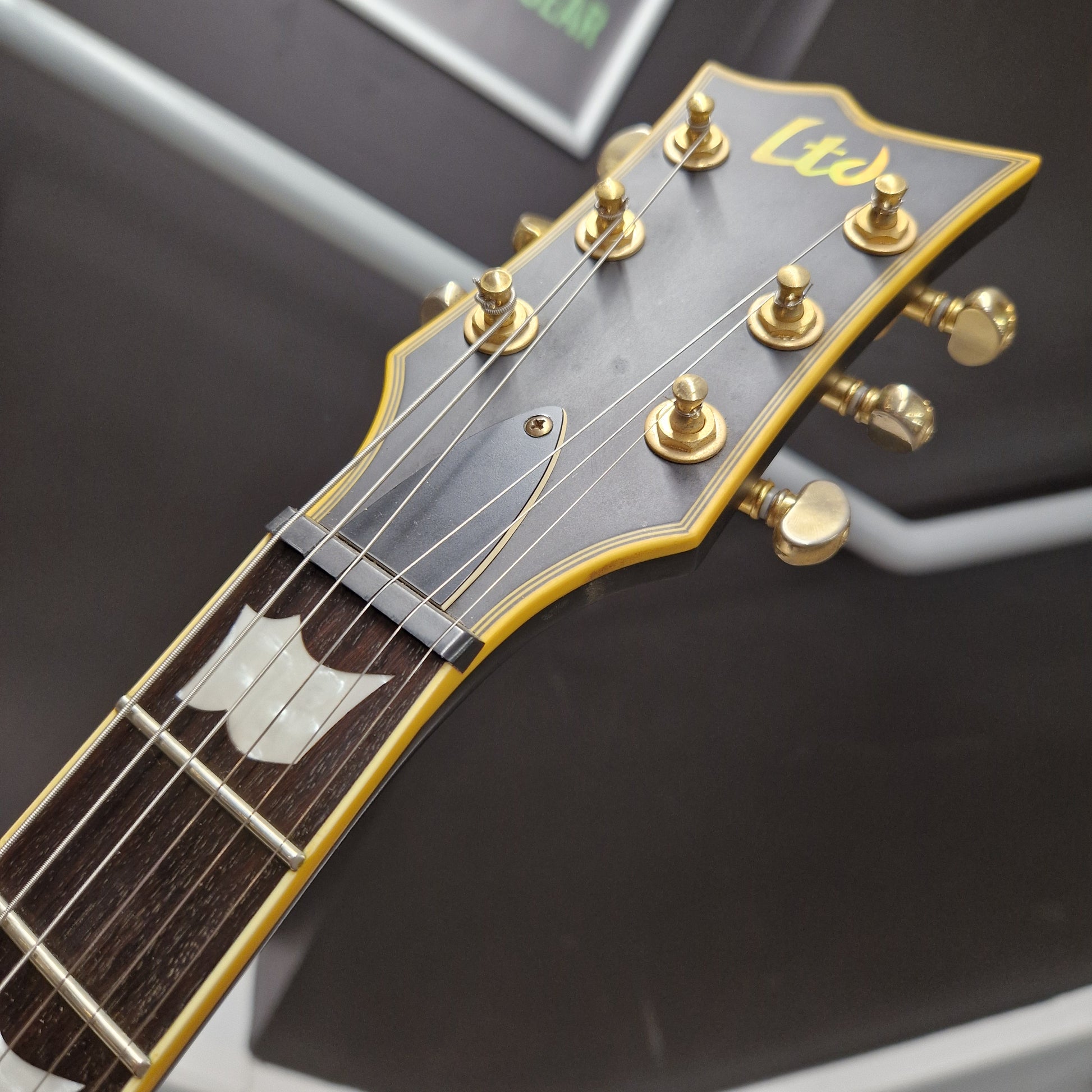 Pre-Owned ESP Close-up of a guitar headstock with gold tuning pegs on a dark background