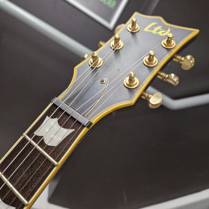 Pre-Owned ESP Close-up of a guitar headstock with gold tuning pegs on a dark background