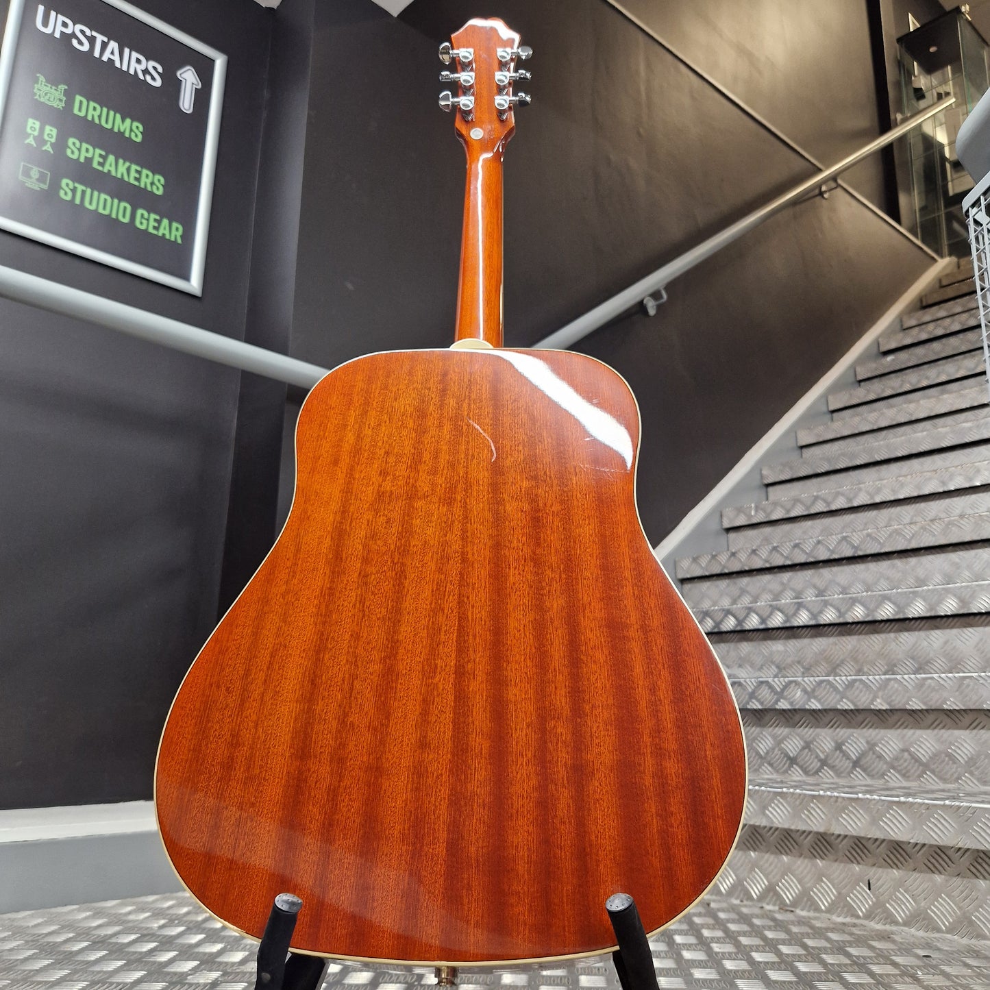 Pre-Owned Epiphone Acoustic guitar leaning against a wall with a metallic surface and text in the background