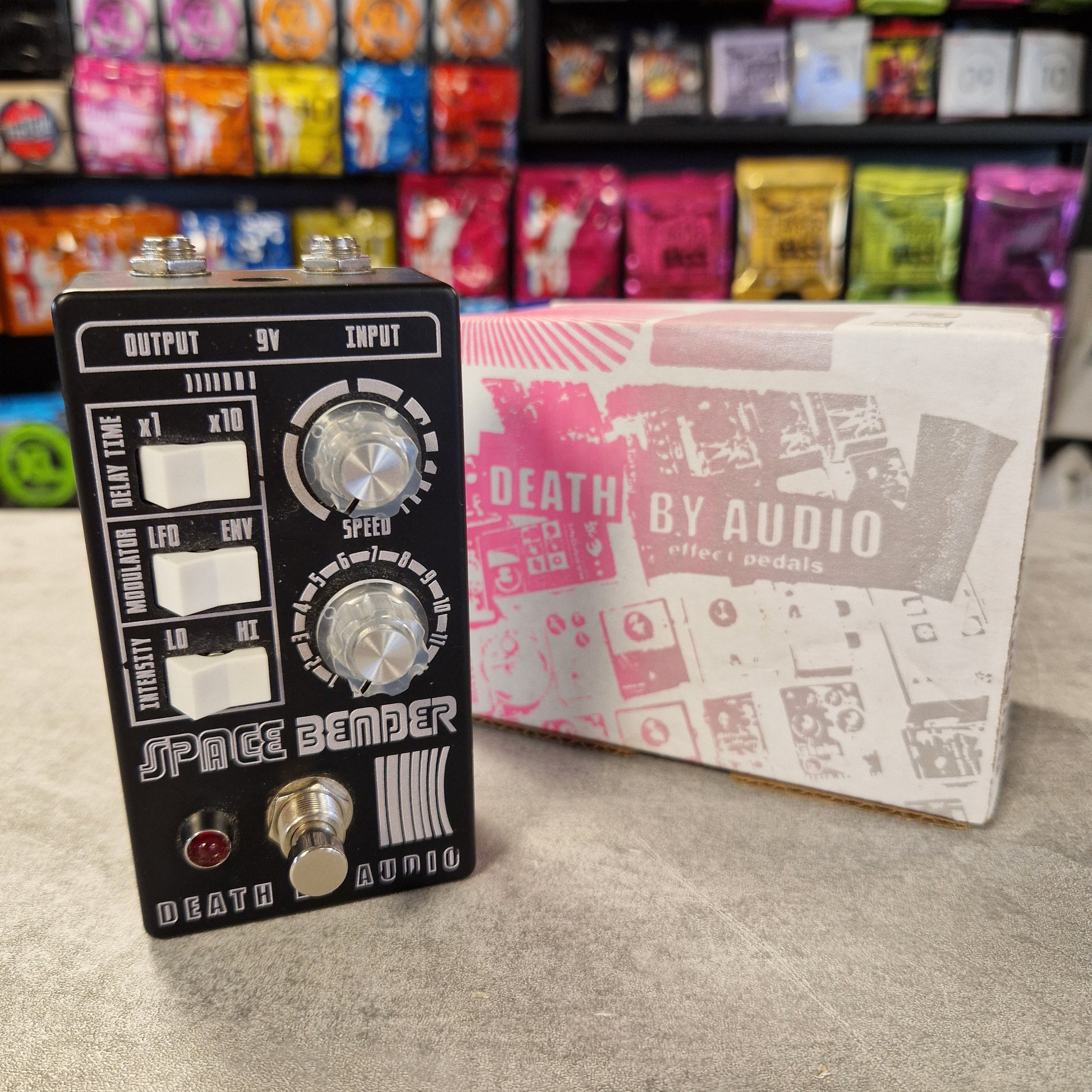 Pre-Owned Death by Audio Guitar effects pedal with 'Space Bender' branding next to its packaging in a store setting.