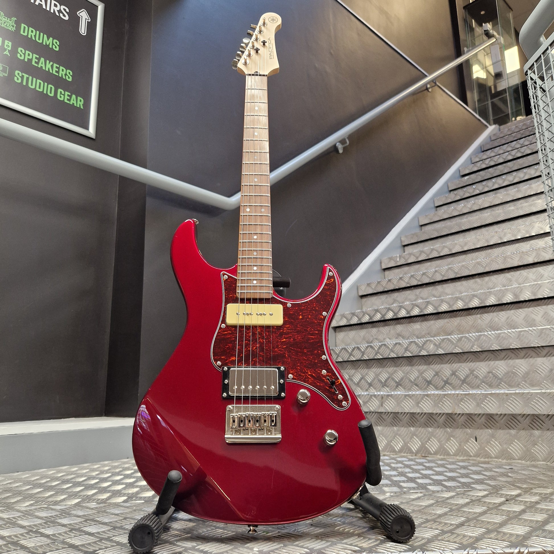 Pre-Owned Yamaha Red electric guitar on a stand in an indoor setting with stairs and signs in the background