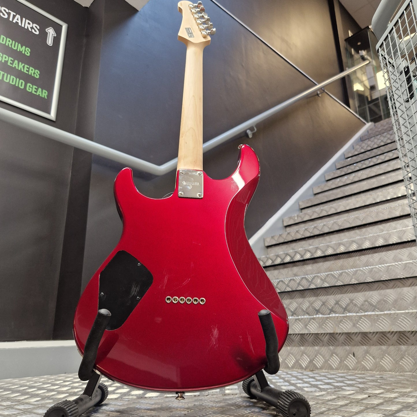 Pre-Owned Yamaha Red electric guitar on a stand in an indoor setting with stairs and signs in the background