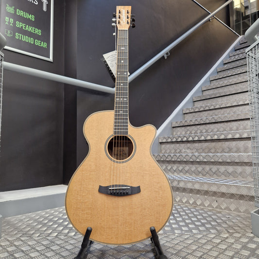 Pre-Owned Tanglewood Acoustic guitar on a stand in front of a staircase with a sign indicating musical equipment.