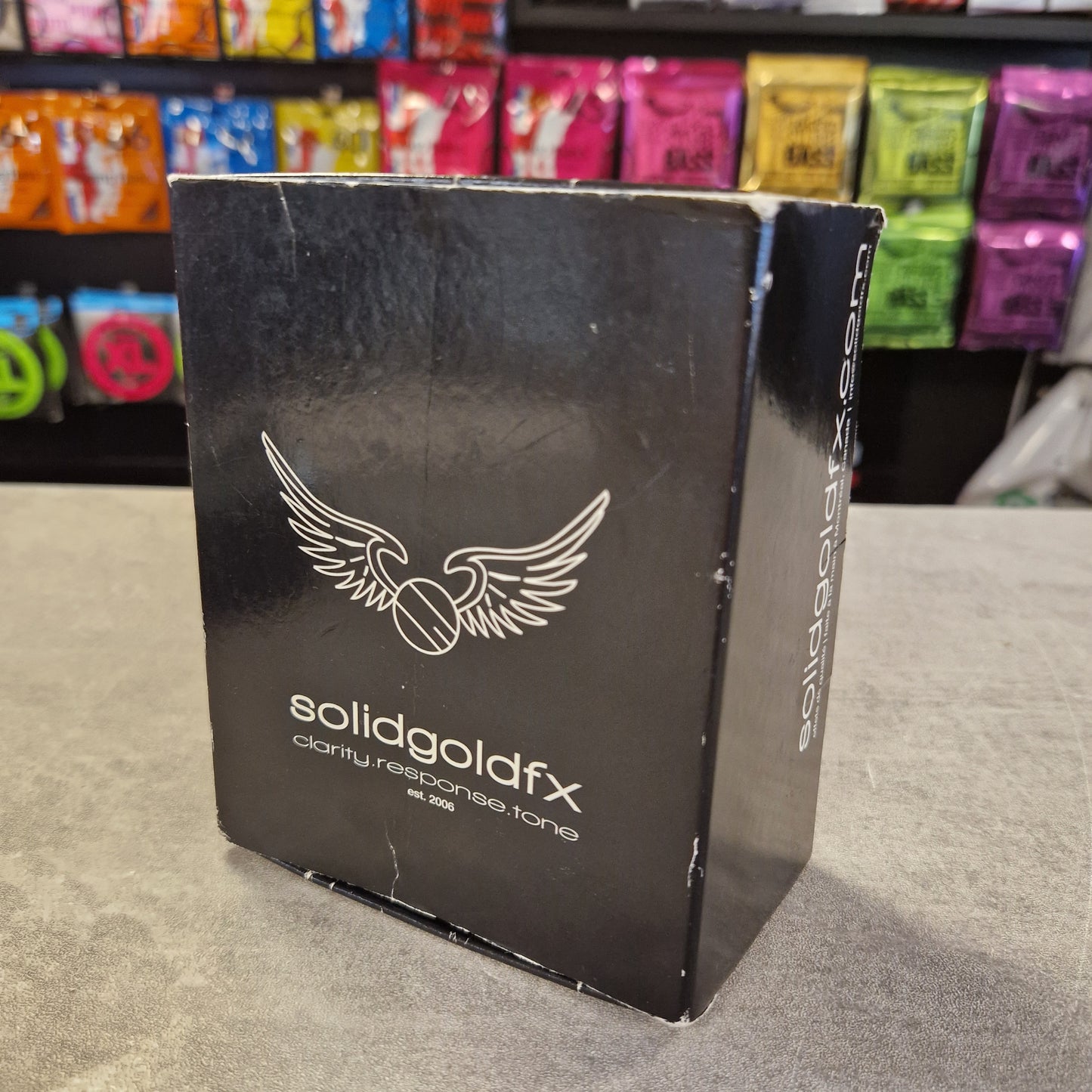 Pre-Owned SolidGoldFx Black box with a logo on a gray surface, with colorful items in the background