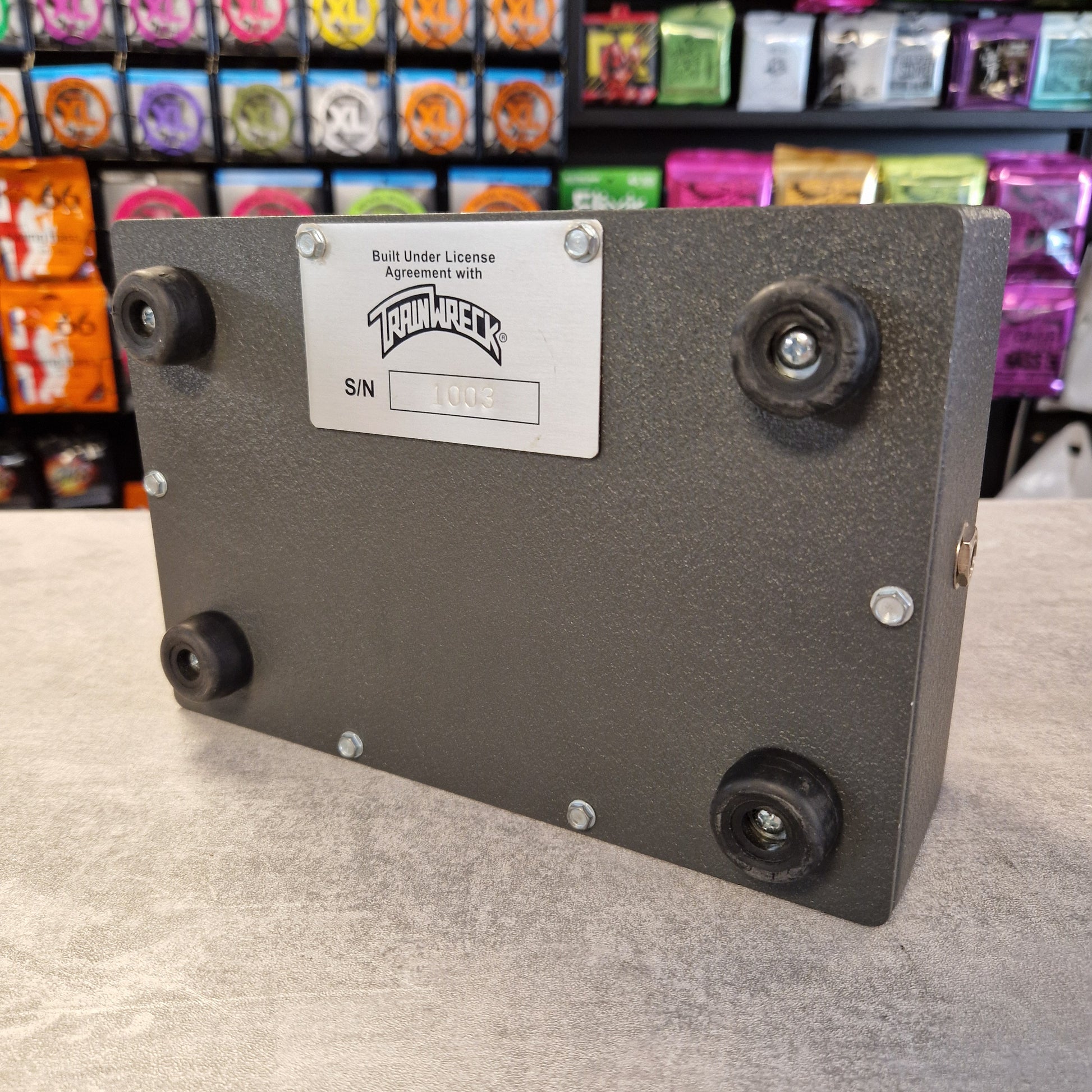 Pre-Owned Dr. Z Trainwreck Black rectangular device with a label on a gray surface, with colorful items in the background.