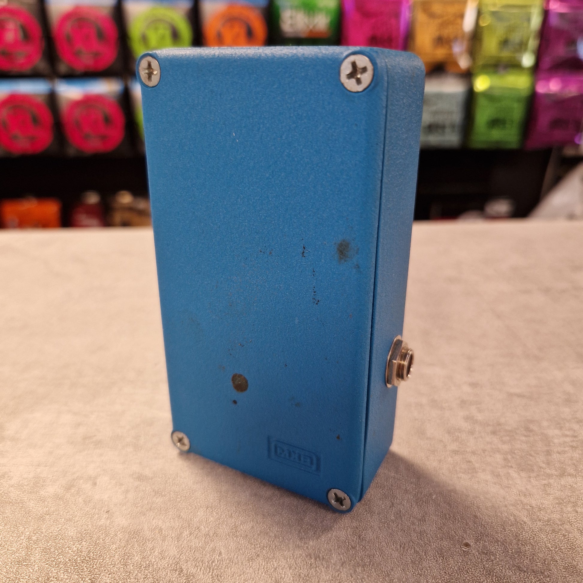 Pre-Owned MXR MX-109 Blue rectangular box with screws on a textured surface, colorful objects in the background