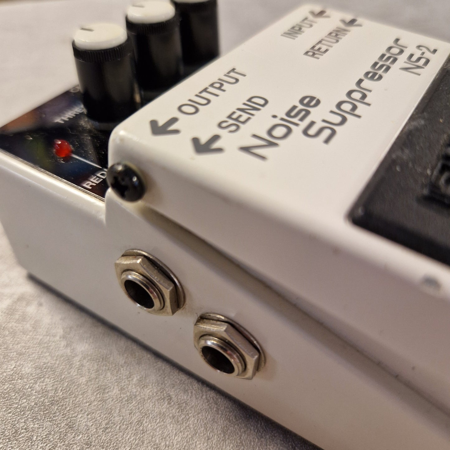 Pre-Owned Boss NS-2 Close-up of a noise suppressor device with labeled ports on a gray surface.
