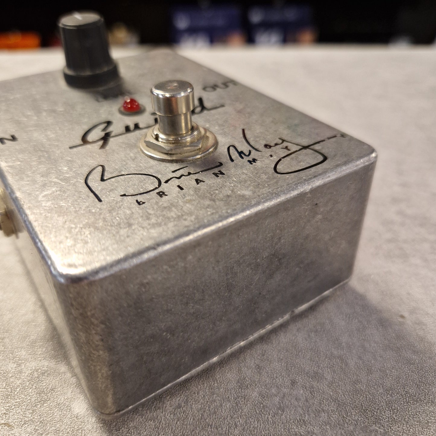 Pre-Owned Guild Brian May Metal footswitch with branding on a blurred background
